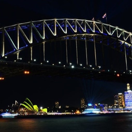 a large bridge lit up at night with Sydney Harbour Bridge in the background